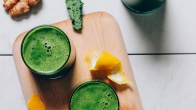 Glasses of homemade Green Juice on a cutting board beside ingredients used to make it