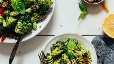 Bowls of Pesto Broccoli Salad beside dry pasta, lemon juice, and sun-dried tomatoes