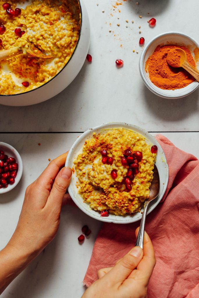 Holding a bowl of Cozy Turmeric Porridge topped with bee pollen and pomegranate seeds